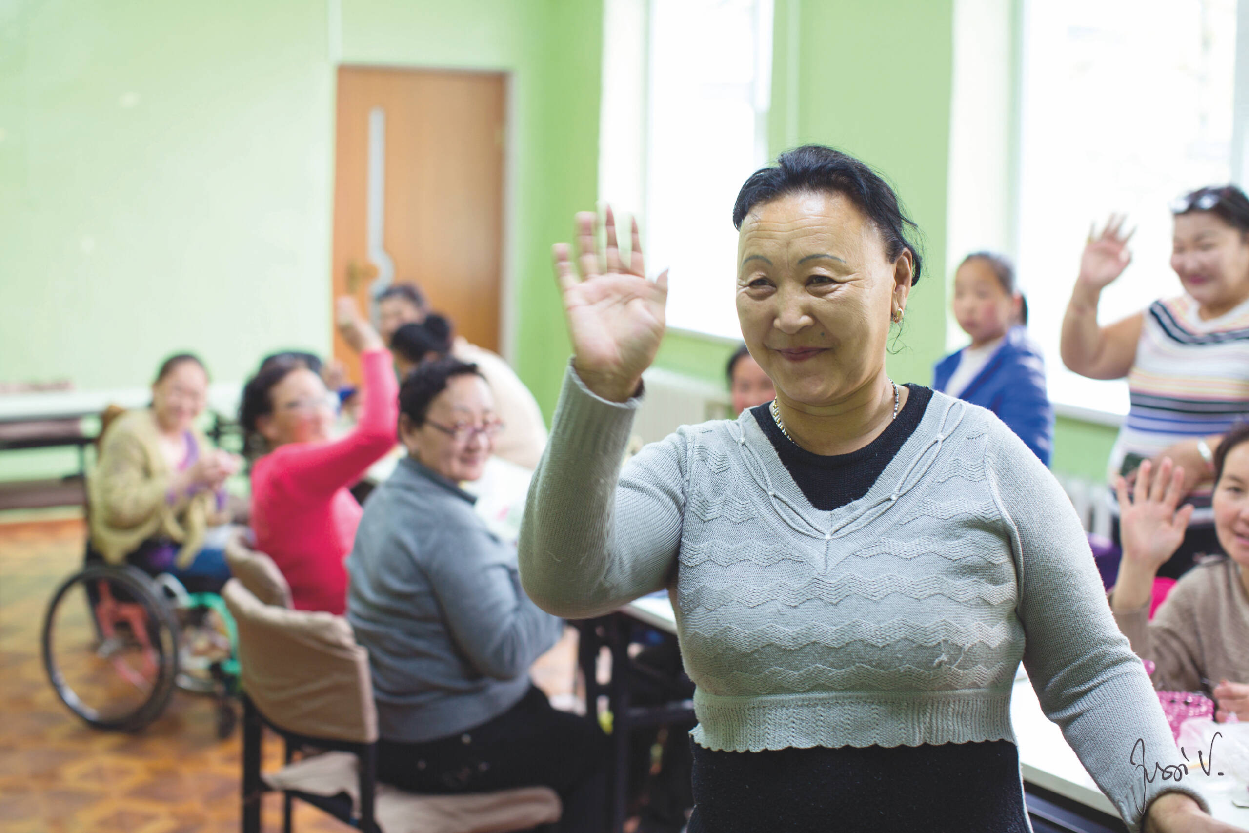 Mongolialainen nainen vilkuttaa iloisesti muiden vammaisten henkilöiden kanssa.