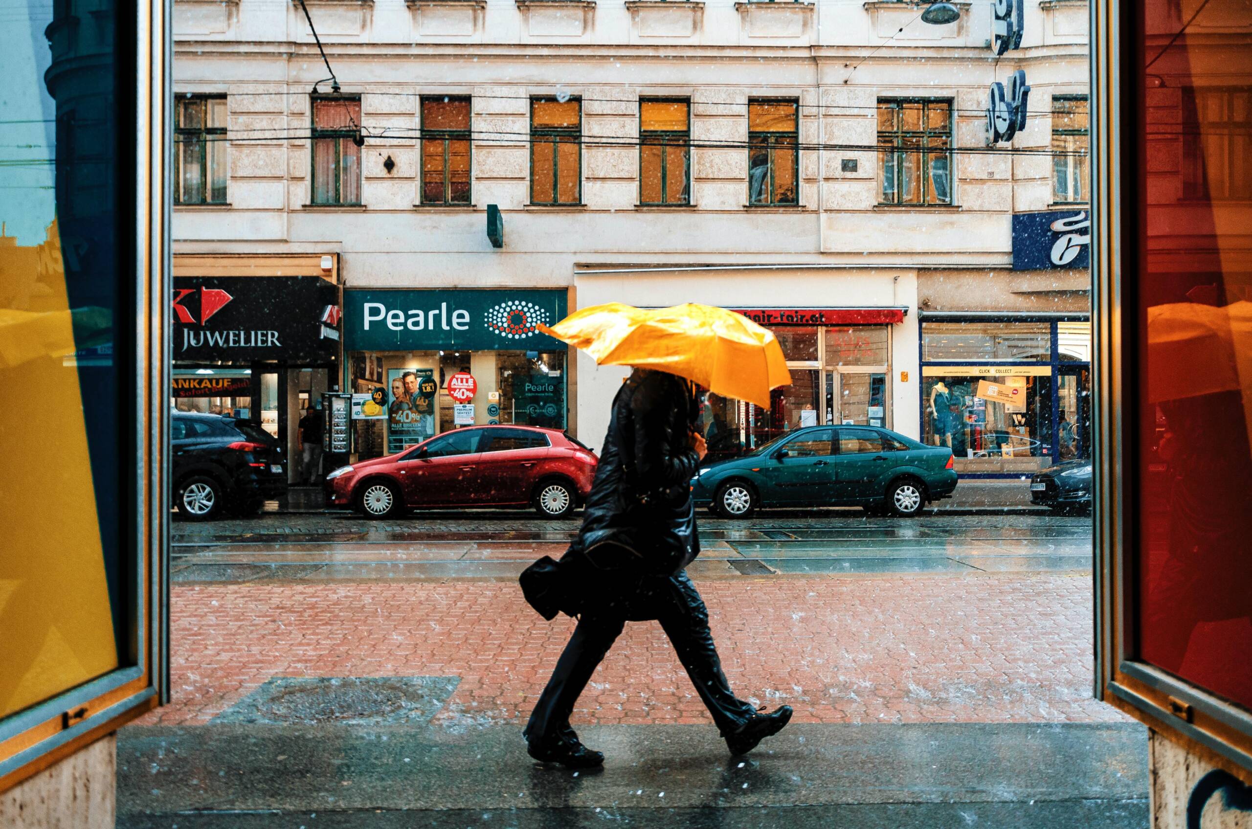 Mies kävelee rivakasti sateenvarjon alla sateisella kaupungin kadulla.