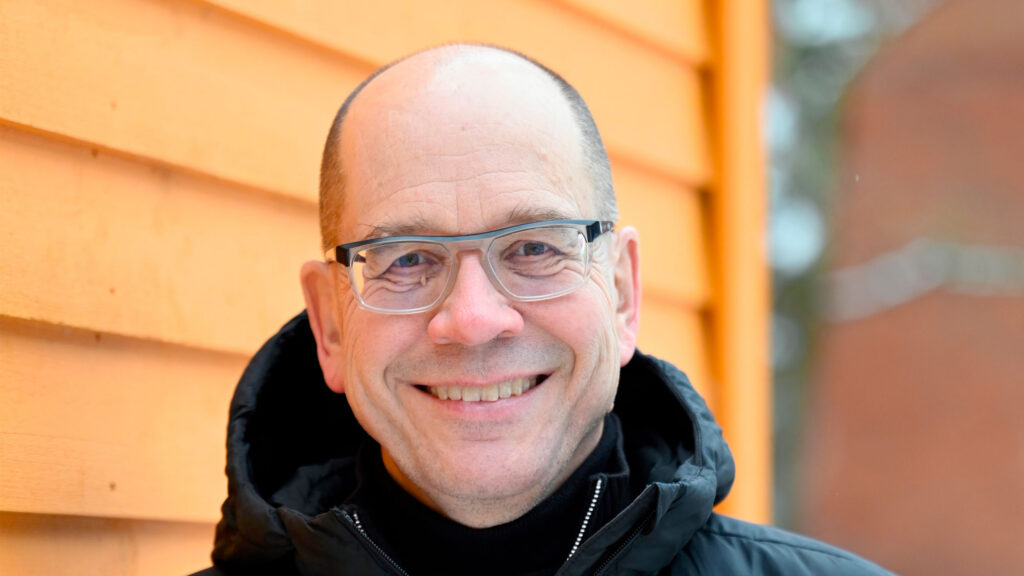 A smiling man outside, orange background.