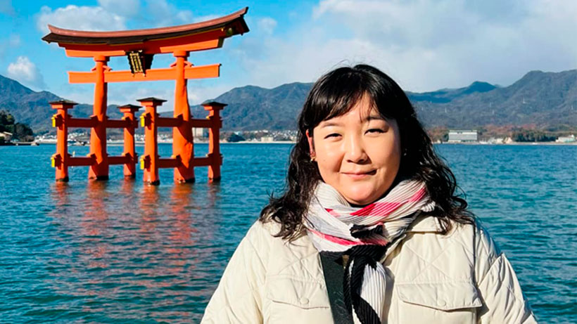 A mongolian woman smiling and looking at camera, in front of a japanese symbol in the water