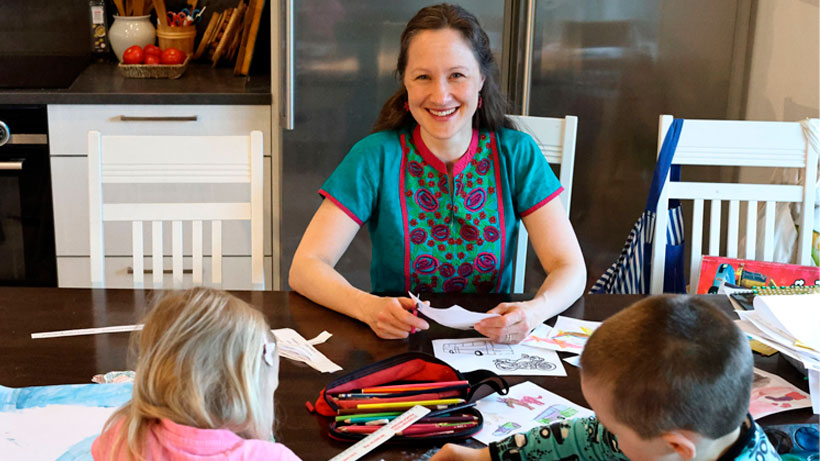 A woman smiling and sitting in kitchen with kids.