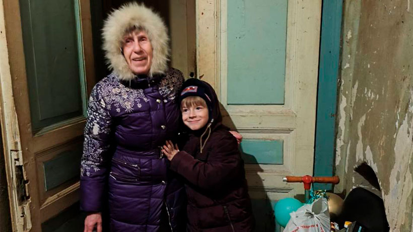 An old woman and a child smiling infront of a door wearing winter clothes.