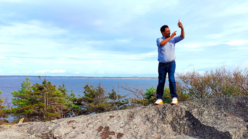A man standing on a cliff and talkin to phone.