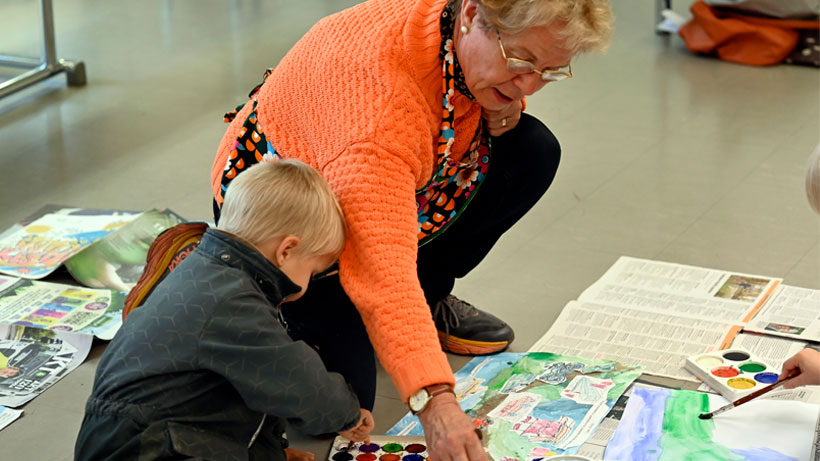 A woman and a child painting with watercolors on the floor.